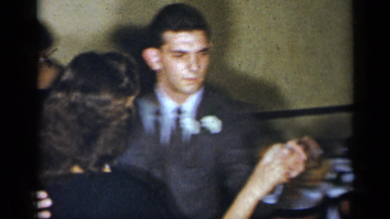 A man in a gray suit with a white boutonniere dances with a woman in an indoor New York social setting from 1954.