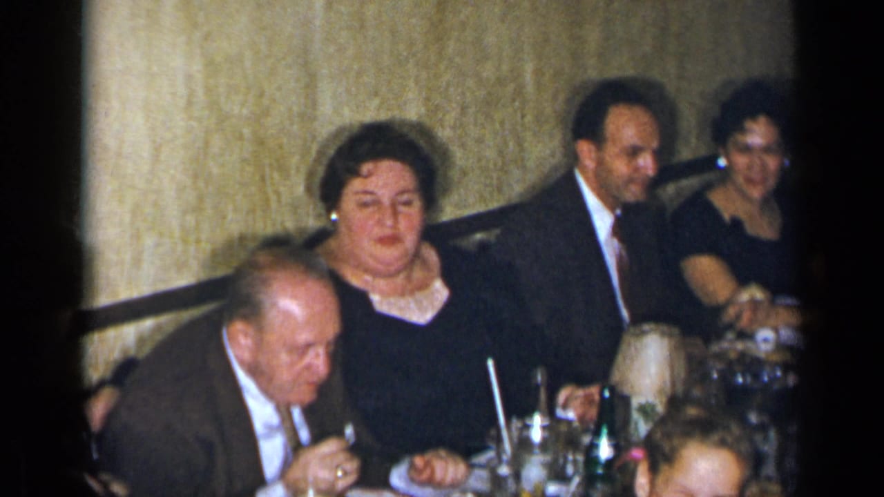 Dinner guests seated beside a textured wall with food and drinks on the table.