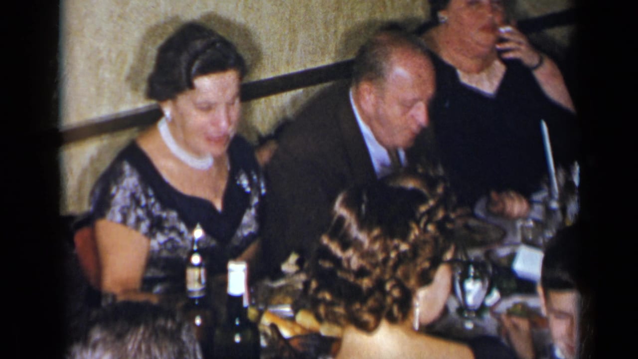 Woman in a patterned formal dress sits at a dinner table beside a suited man.