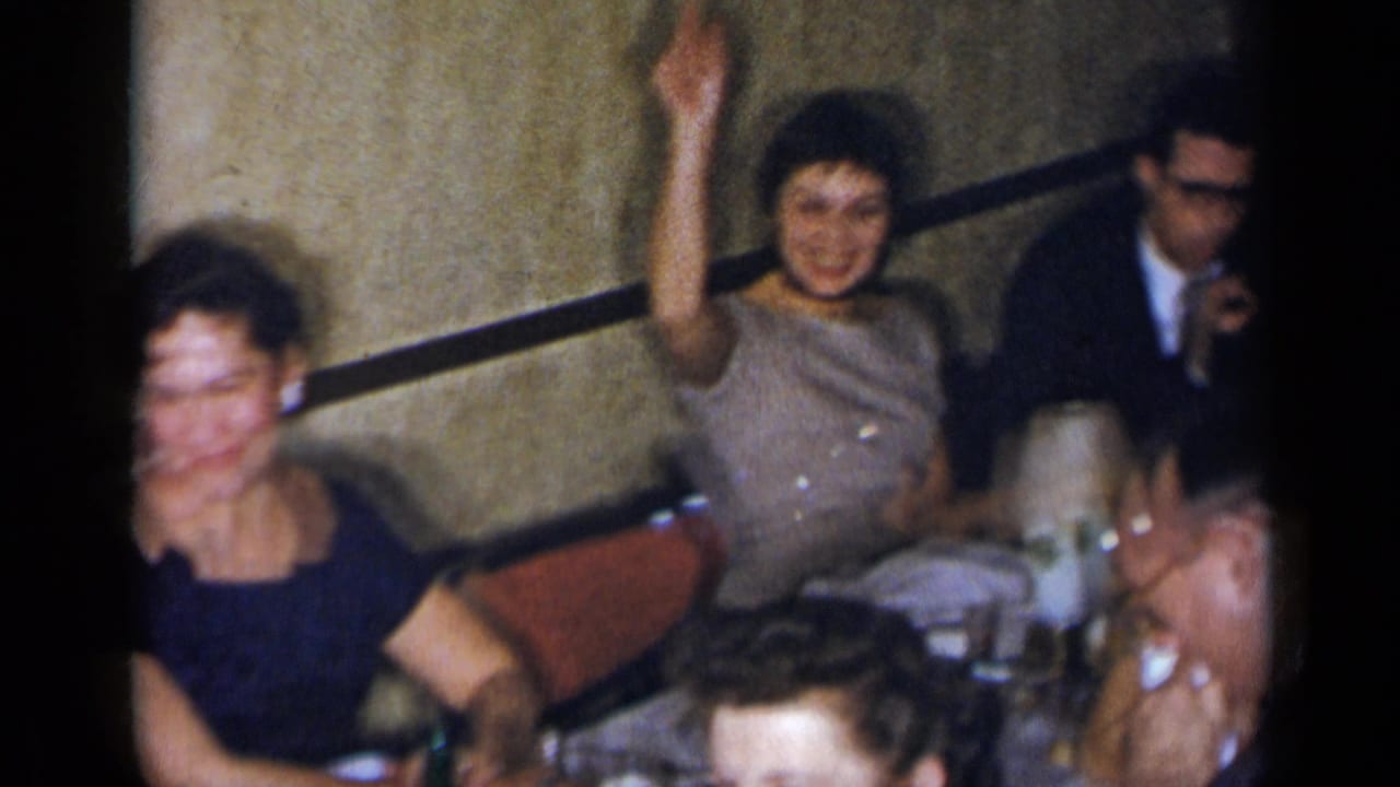 Several adults sit around a table while one woman raises her hand.