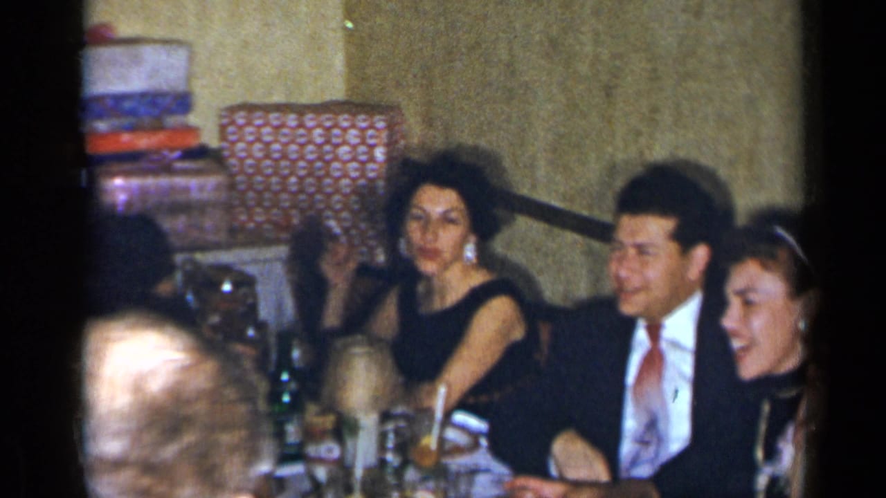 Adults in formal clothing sit at a table during an indoor gathering.