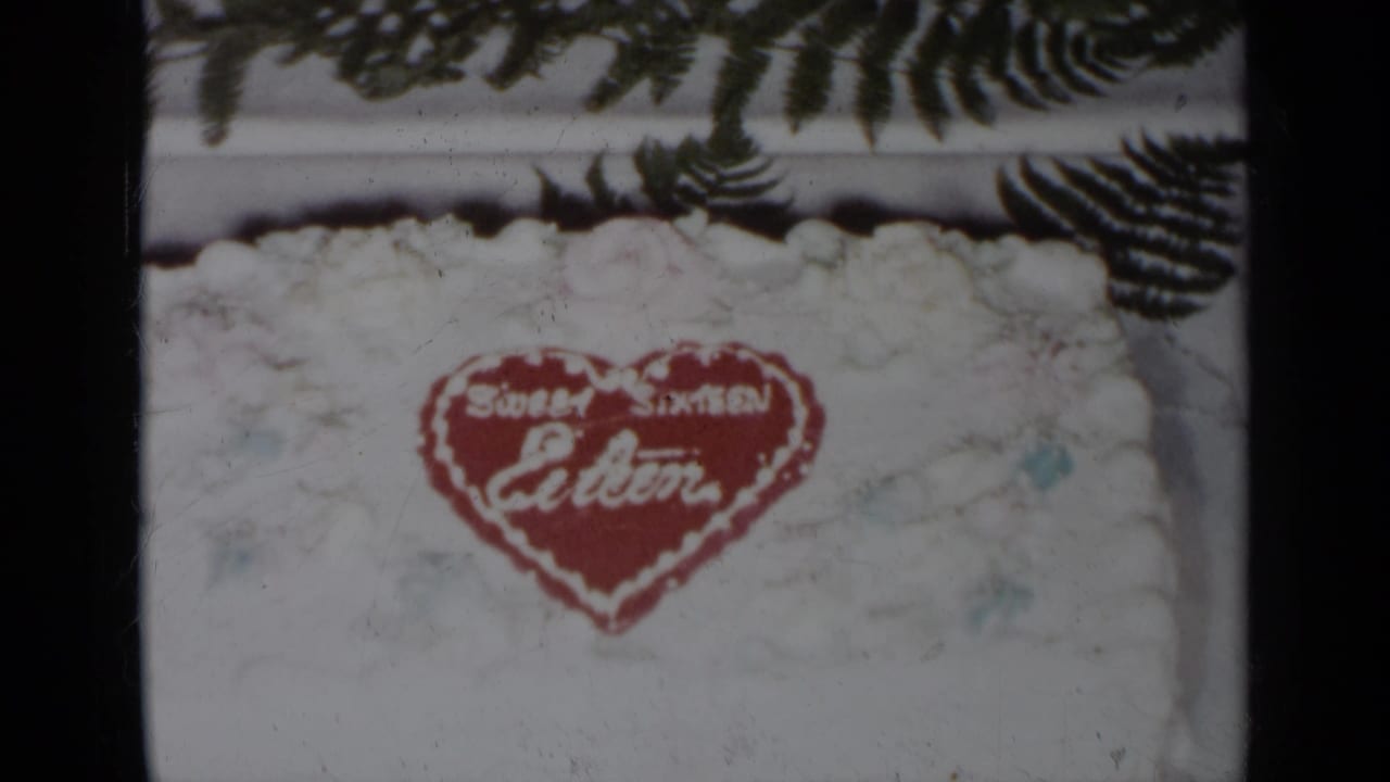 Red heart decoration on a white frosted cake, with fern leaves visible above.