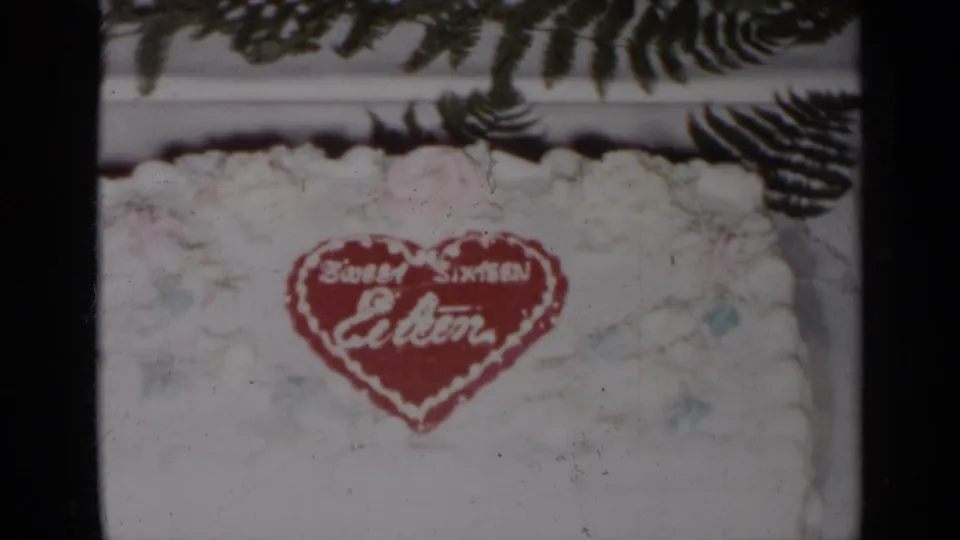 1954 New York 8mm close-up of the Sweet Sixteen Eileen cake decoration beneath dark fern leaves.