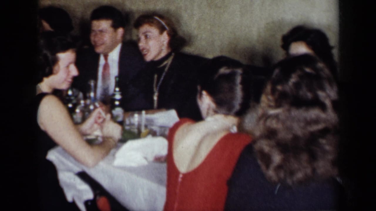 Dinner guests seated close together at a table with bottles and glasses.