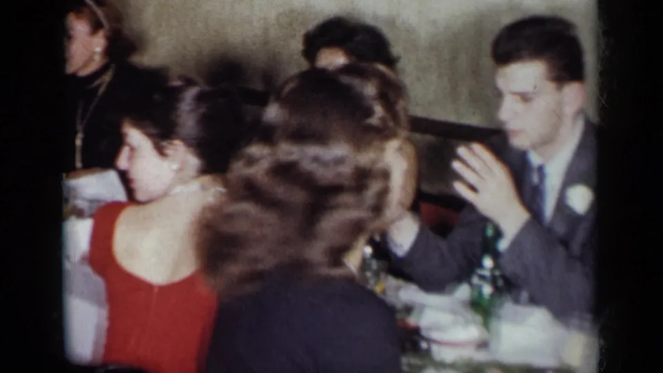 A 1954 New York dinner-party frame shows guests in formal clothing, with a suited man near the table and women seated in the foreground.