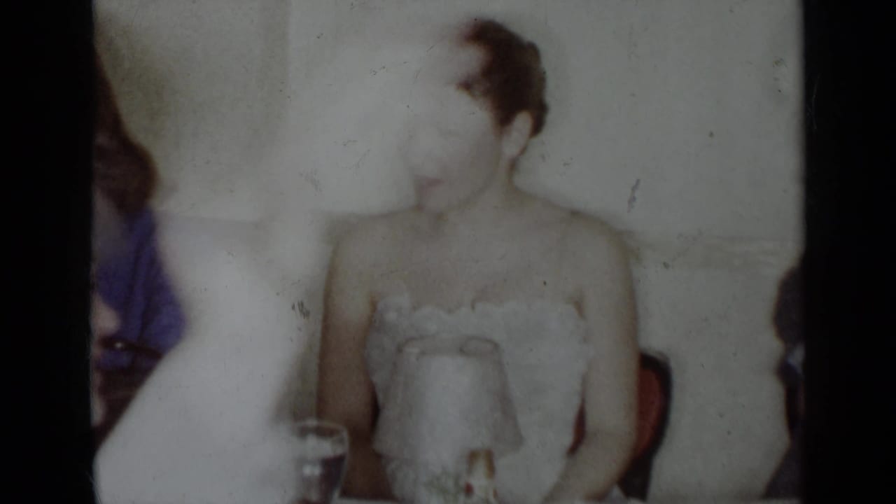 Woman in a strapless white dress sits at a table beside other guests.