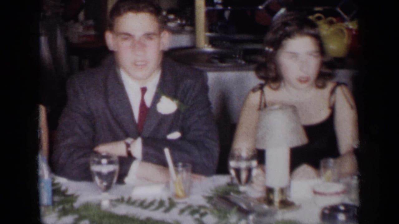 Young man in a suit and woman in a black dress seated at a formal table.