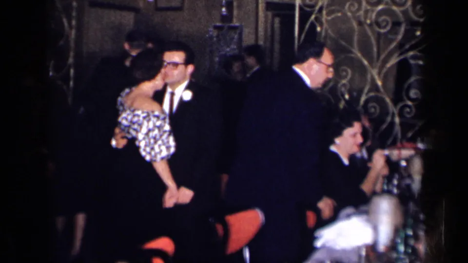 1954 New York home-movie frame showing guests in suits and patterned dresses dancing in a crowded interior.