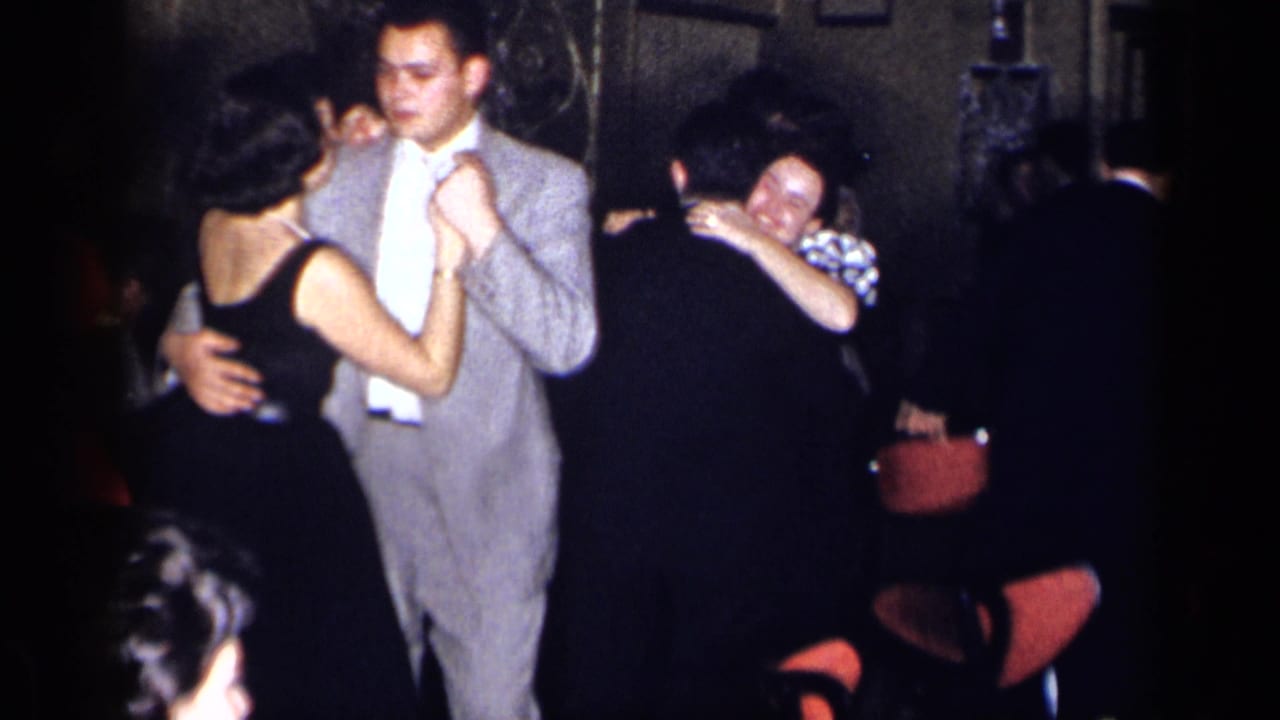 Adults dance closely at a 1954 New York indoor party, with a man in a light gray suit and women in dark dresses visible.