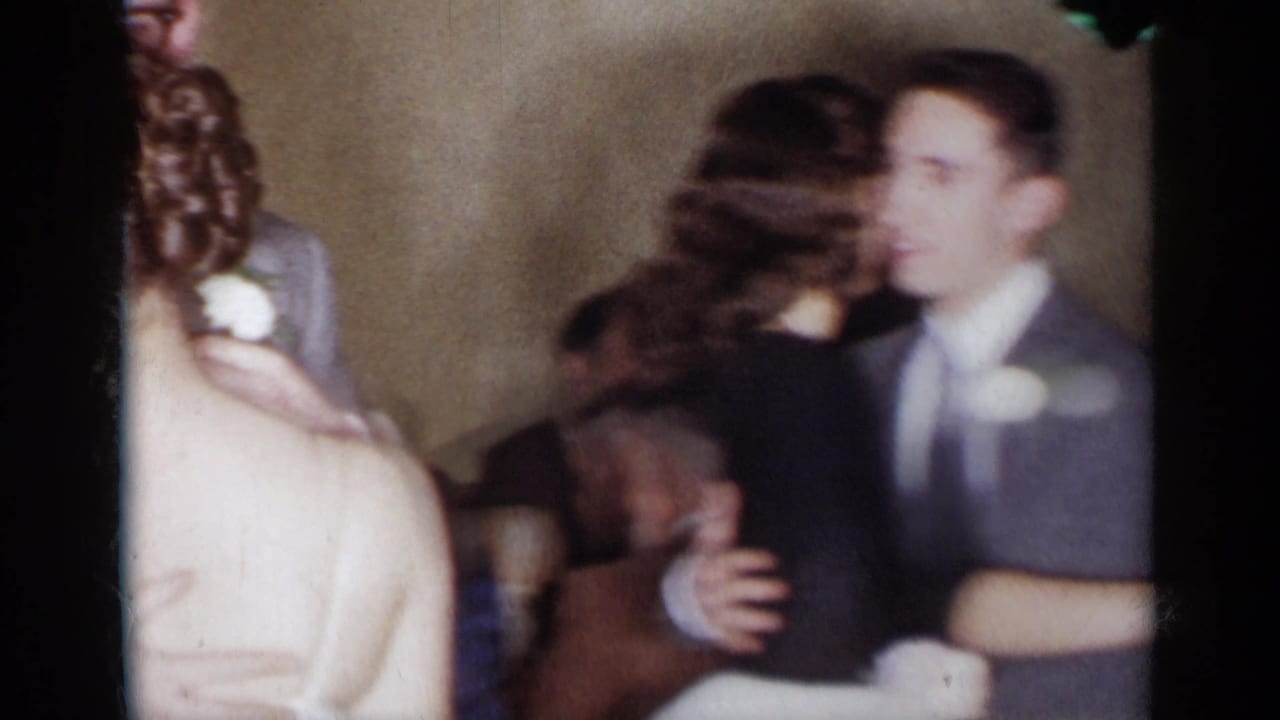 Couple dancing closely in a dim room with another guest partly visible at the edge.