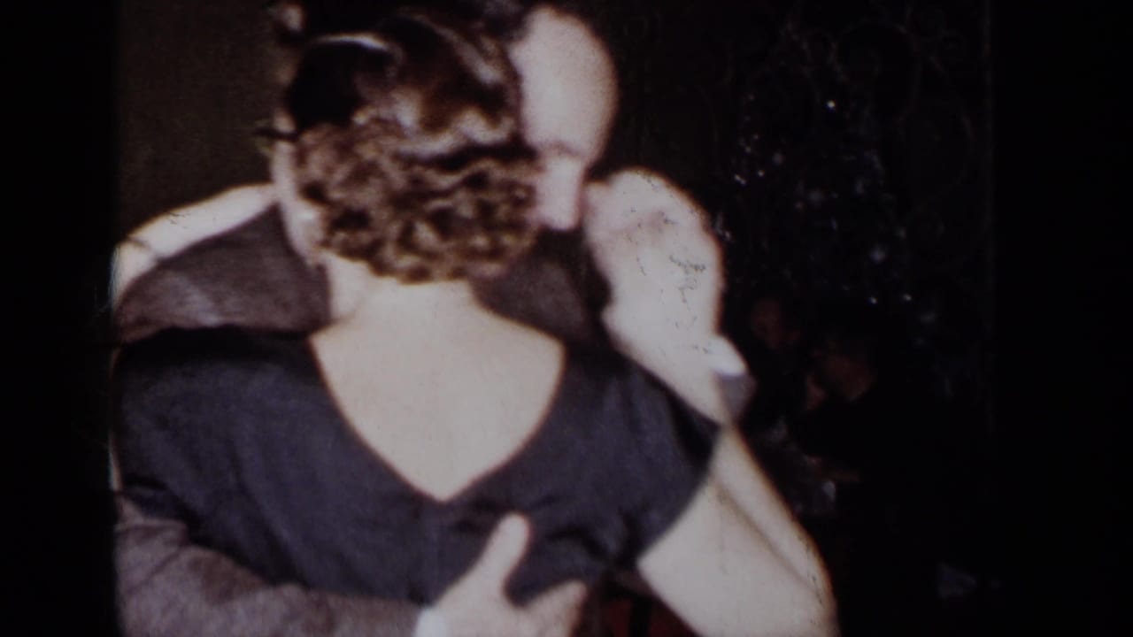 Man and woman embrace while dancing, seen from behind in a dark indoor room.