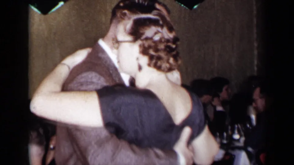 A close view of the dancing couple shows formal dress and seated guests at tables in the background of the 1954 New York party.