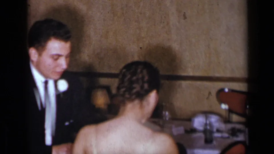The final frame keeps the couple in a private indoor formal setting, with chairs and tableware visible behind them.