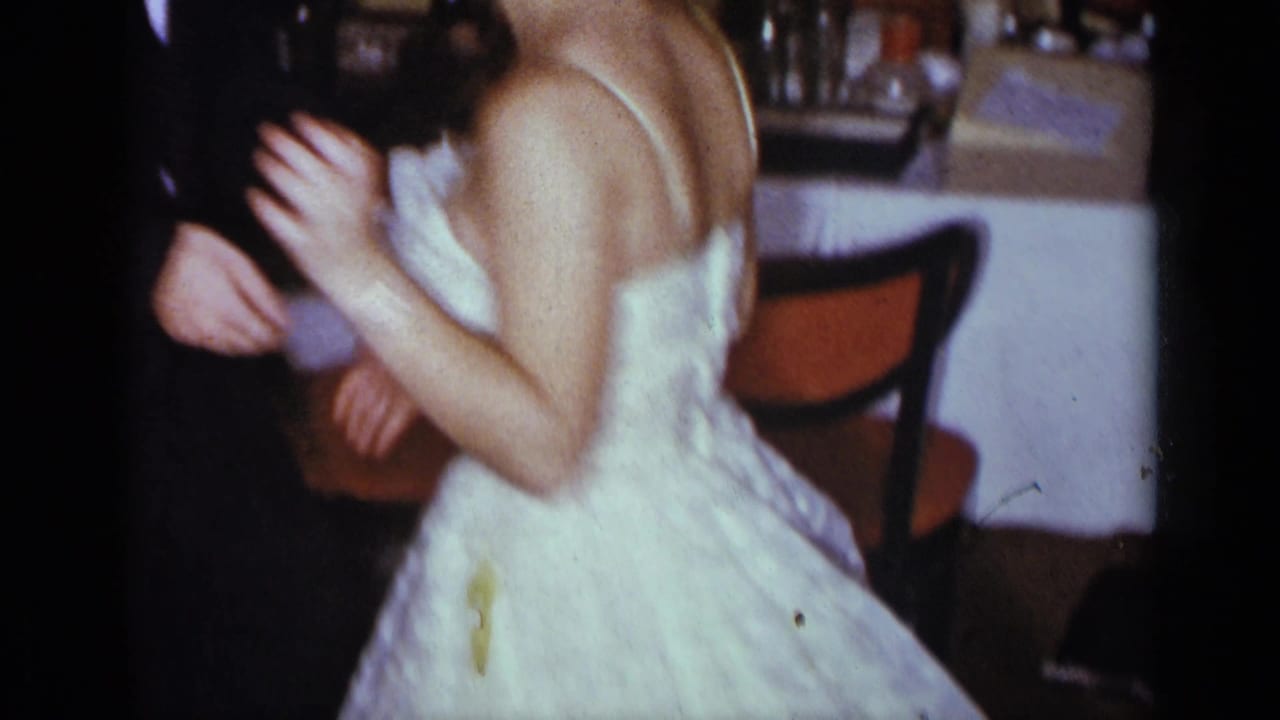 The bride's strapless white gown fills the frame as she dances with the groom in a dim banquet hall setting.