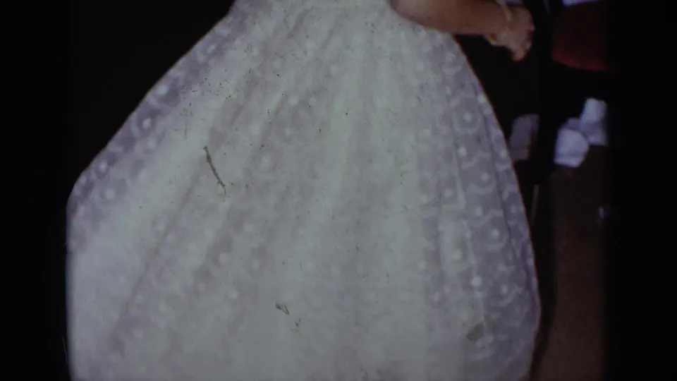 A close handheld view centers on the bride's full white wedding skirt as movement continues in the reception room.