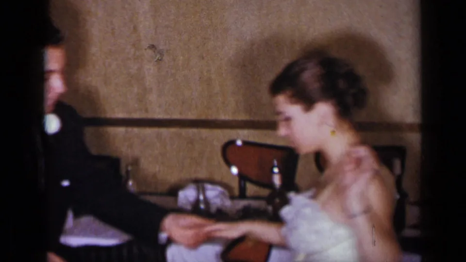 In 1954 New York home-movie footage, a formally dressed couple sits close together at a table in a warm indoor room.