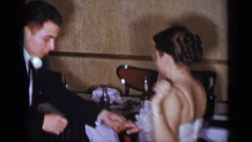 The couple appears in a candid 1954 New York interior moment, with the woman turned away and the man leaning near the table.