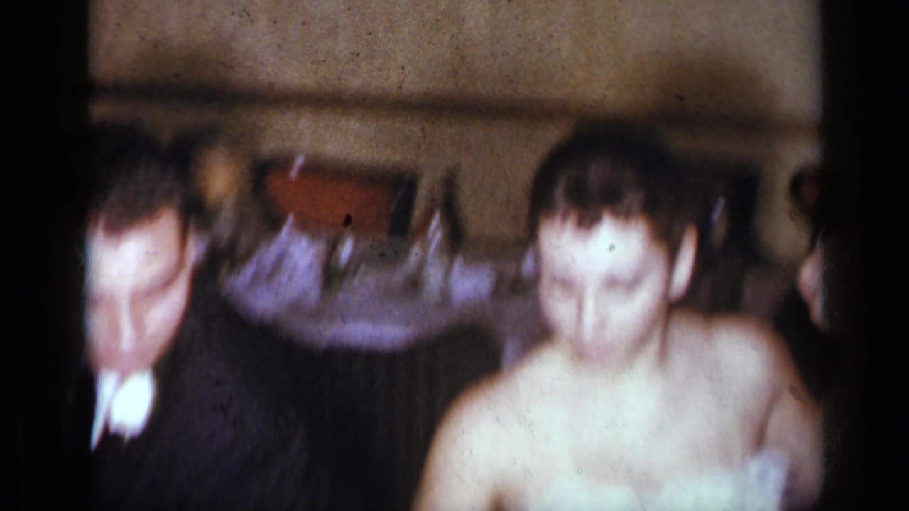 Blurred man in dark suit beside woman in light formal dress indoors.