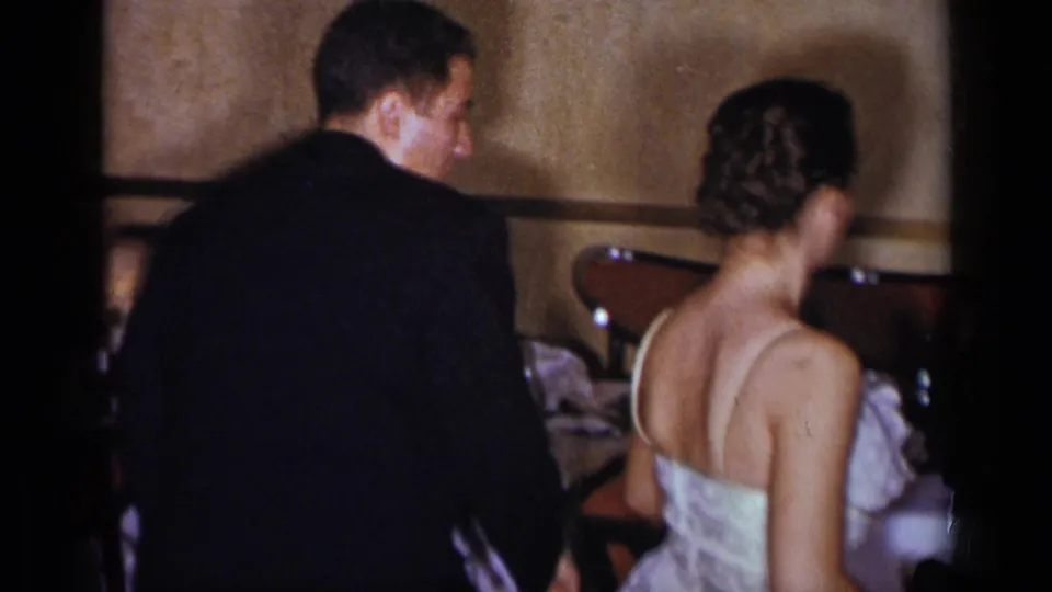 A suited man and woman in a light formal dress stand close together inside a 1954 New York event space.