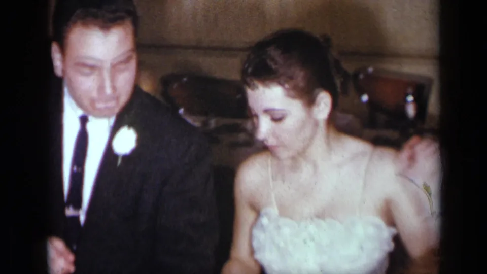 The couple appears in closer view, with the man in a dark suit and boutonniere beside a woman in a light strapless dress.