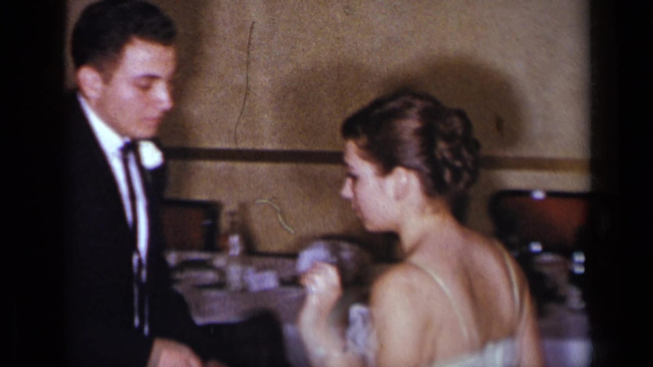 Young man in a tuxedo faces a woman in a strapless light dress inside a restaurant.