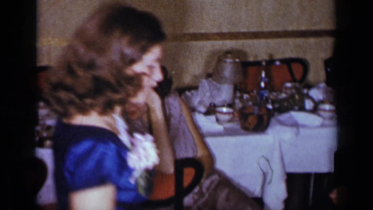 Woman in a blue satin dress with a white corsage turns in front of a dinner table.