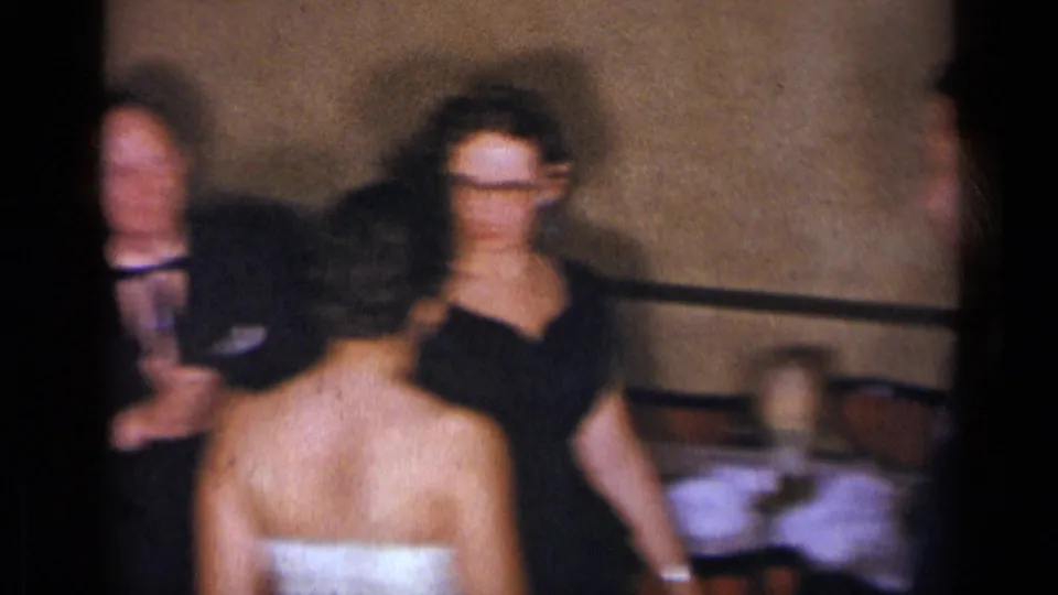 1954 New York wedding reception frame showing the bride from behind as older guests stand or sit nearby in soft focus.