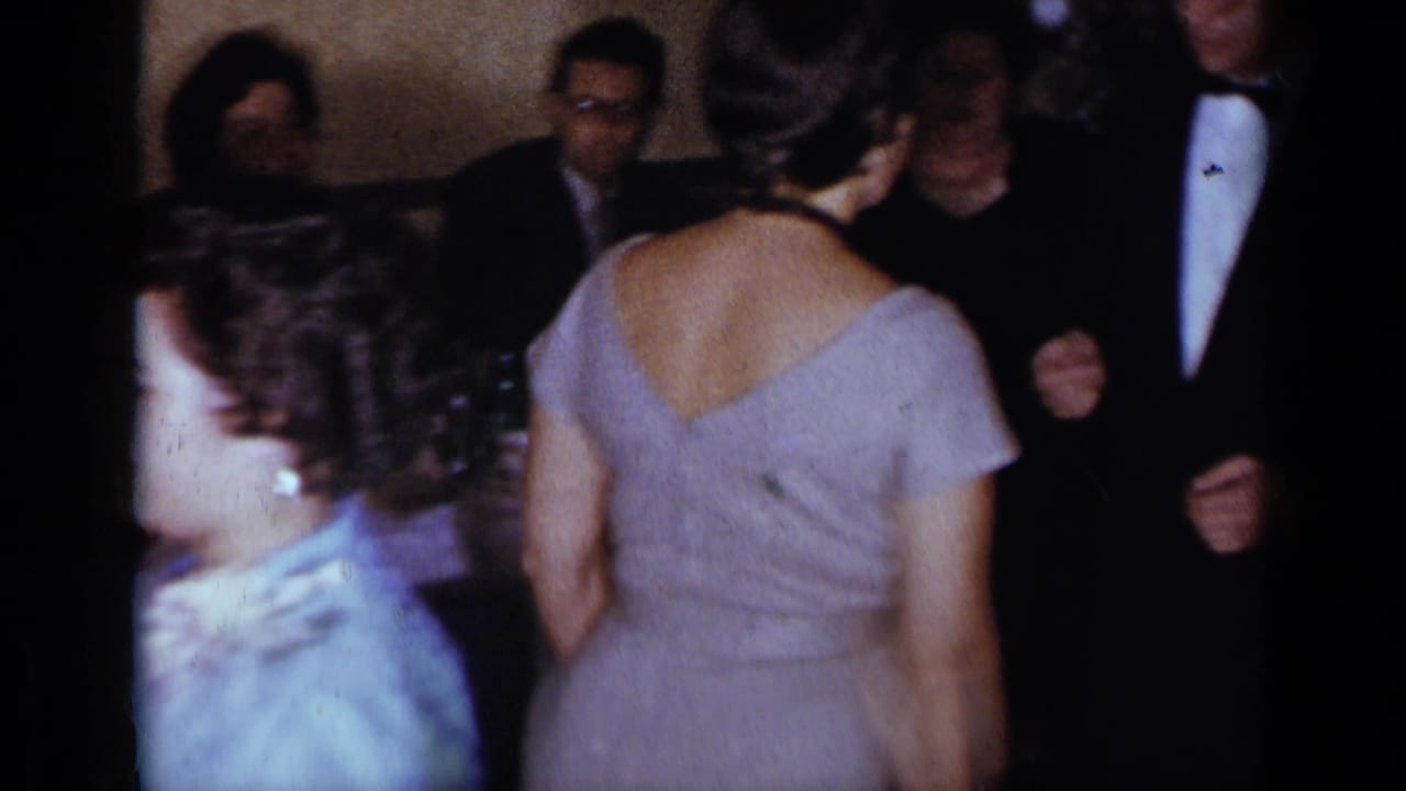 Adults in formal clothing gather in a decorated interior before dancing.