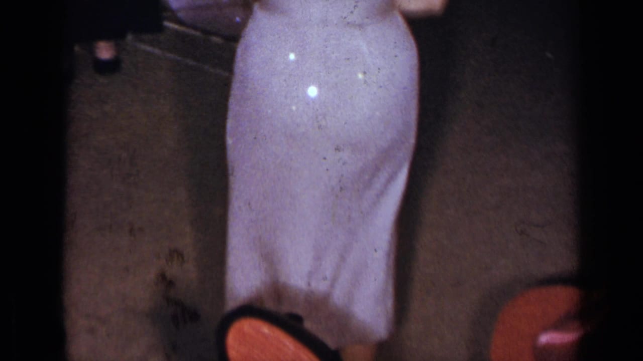 Cropped view of a woman in a pale dress standing near red chairs indoors.