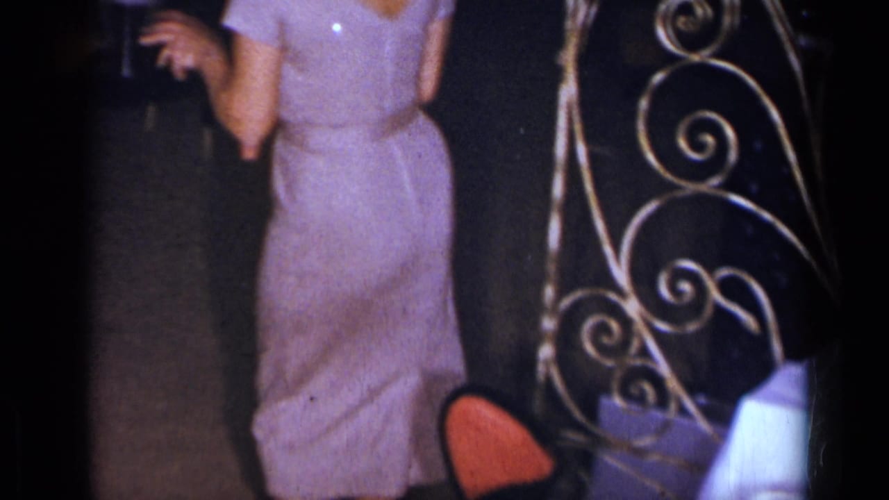 1954 New York home-movie frame showing a woman in a sparkly purple dress dancing near decorative metal scrollwork.