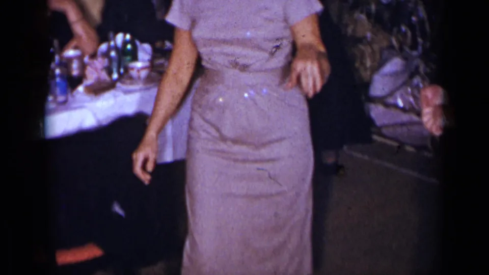 1954 New York home-movie frame with a closer view of the woman's dress as she dances near seated guests and a set party table.