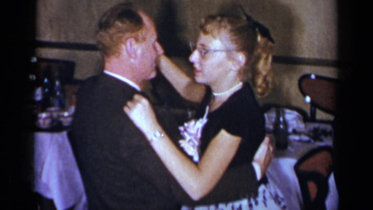 Man in a dark suit and woman in a black dress dancing near dining tables.