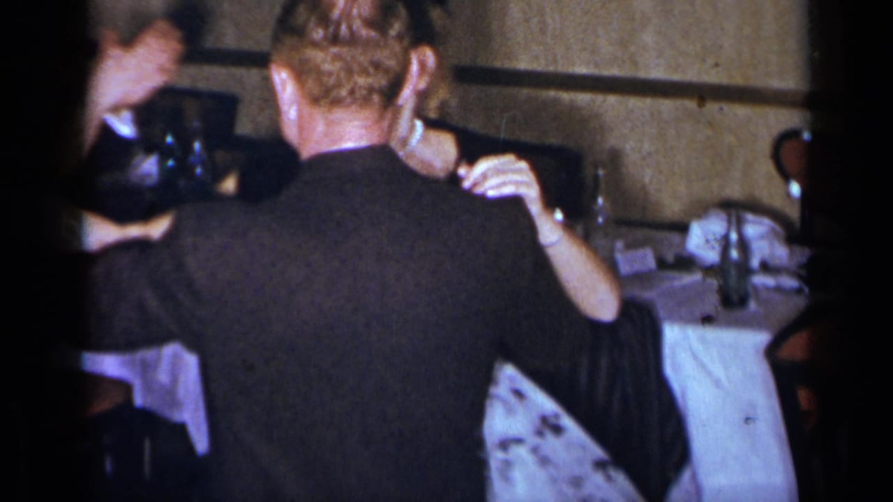 Couple seen from behind while dancing beside tables and chairs.
