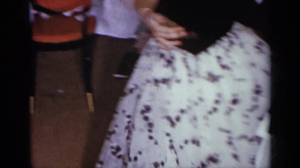 Close home-movie view of the dancing couple, centered on the woman's white patterned skirt and the man's arm.