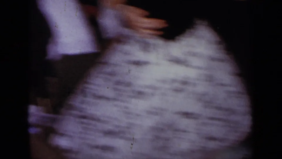 Soft, motion-blurred 1954 home-movie frame of the couple dancing close, with the woman's full skirt filling the foreground.