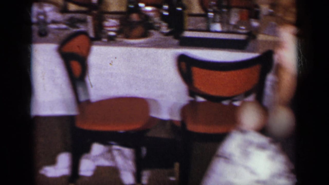 Tables with white cloths, orange chairs, glassware, and blurred guests in a dim hall.