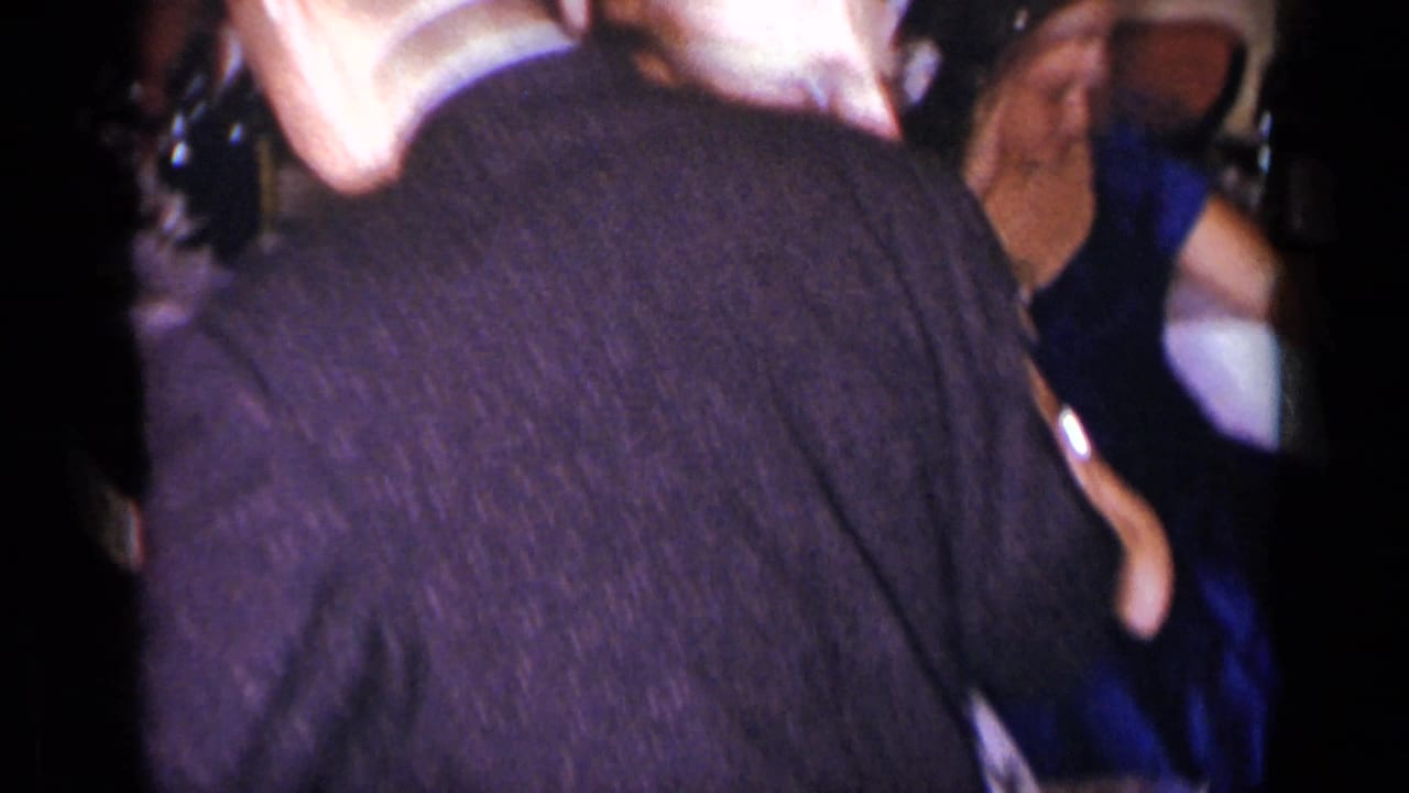 Close handheld view of a suited man dancing with a woman in a dark dress.