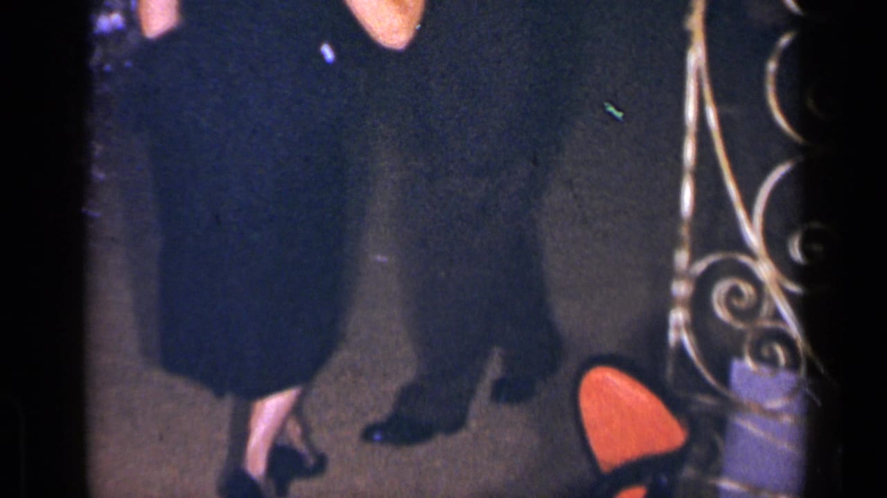 Partial view of dancers' legs, dark formal clothing, polished shoes and ornate metalwork in a dim interior.