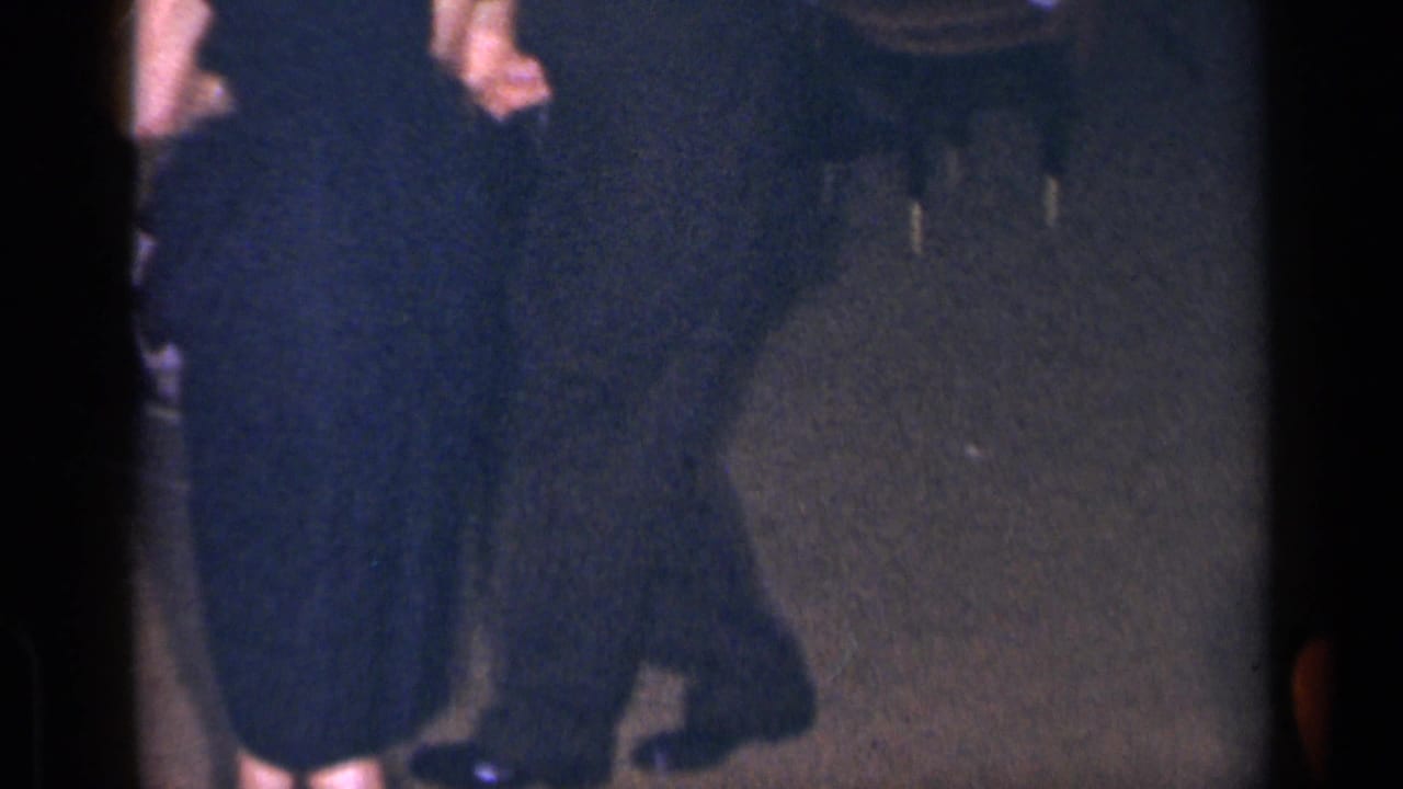 Cropped lower-body view of adults in dark formal wear standing or dancing on a dim floor.