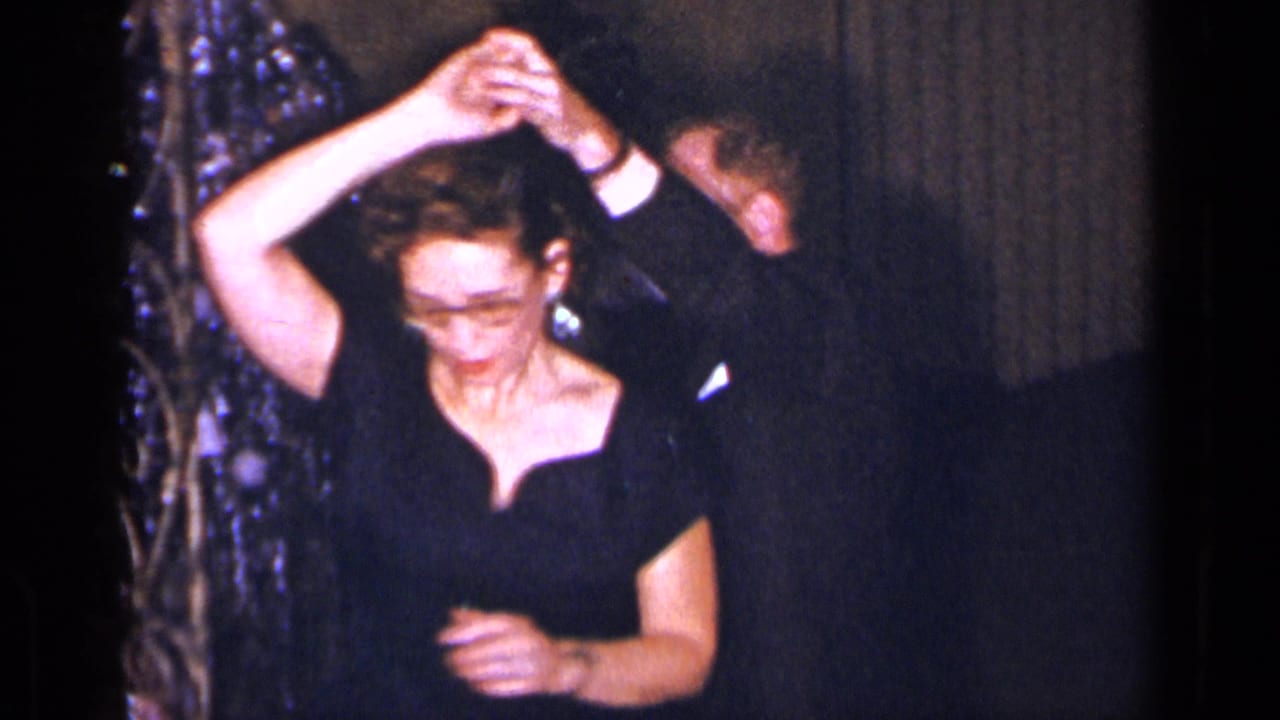 Woman in a black gown turns under a raised hand while dancing with a man partly out of frame.