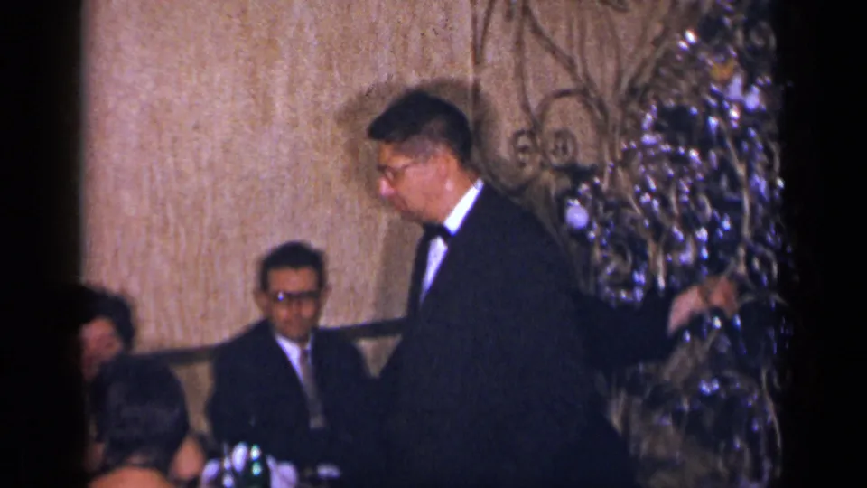 At the same 1954 New York social gathering, suited men converse near a table while one stands beside decorated interior branches.