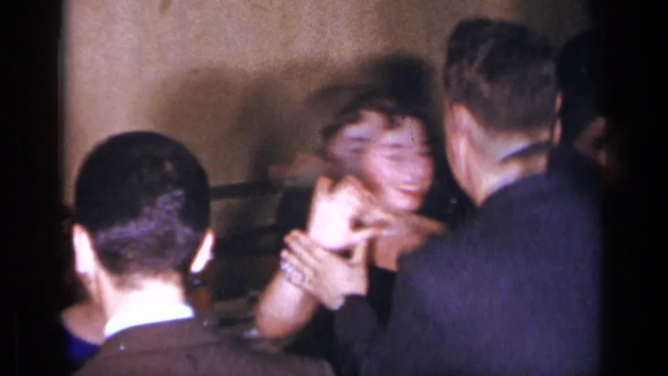 1954 New York home-movie frame showing a smiling woman dancing closely with a man in a dark suit at an indoor gathering.