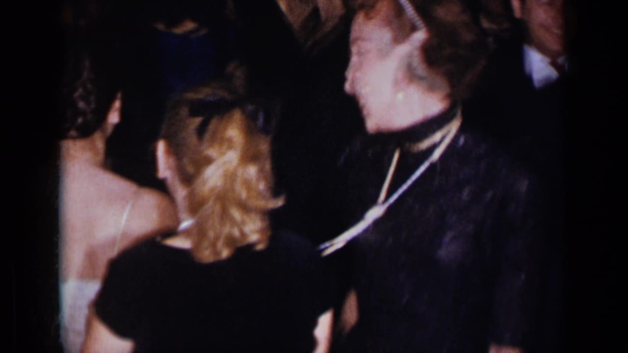 Crowded formal gathering with women in dark dresses seen from behind and in profile.