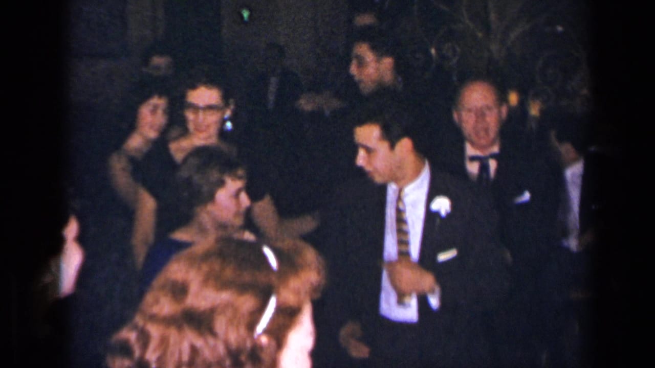 Men and women gather on a dance floor, with one man wearing a boutonniere.