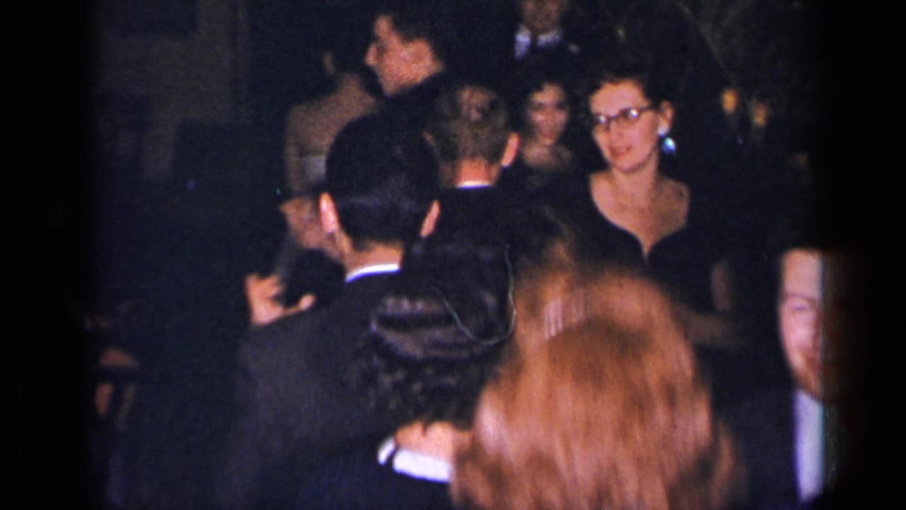 Adults in formal clothing dance in a dim, crowded interior.
