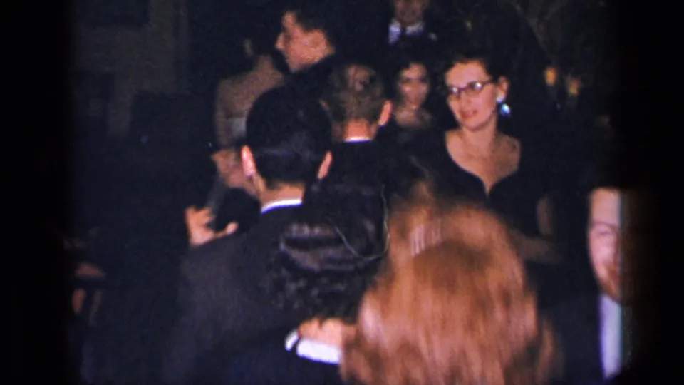 1954 New York home-movie frame showing adults in suits and dresses dancing in a crowded dim interior.