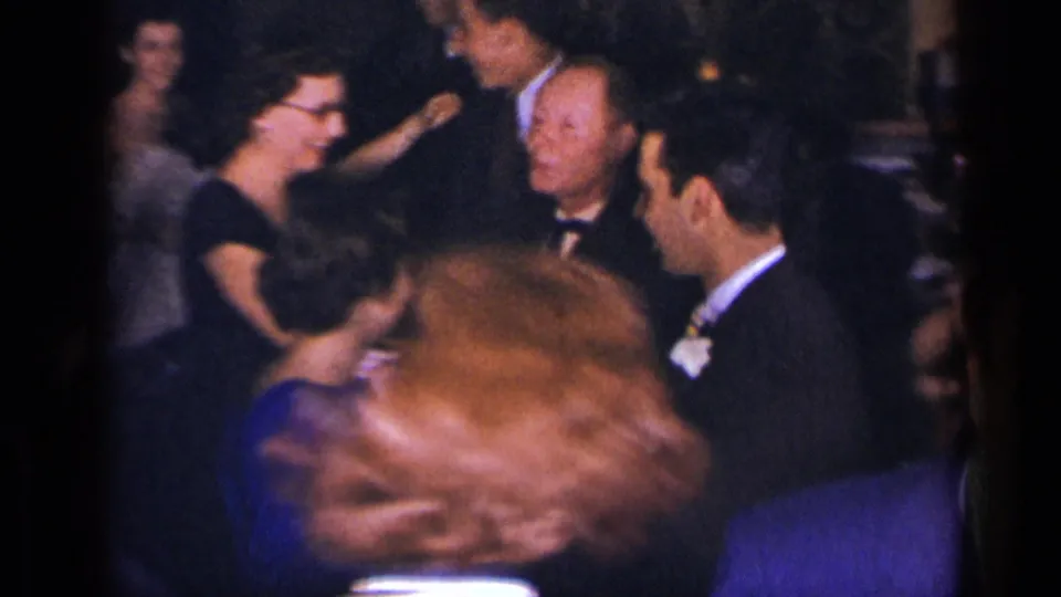 1954 New York party scene with suited men and women in dresses gathered and dancing in low light.