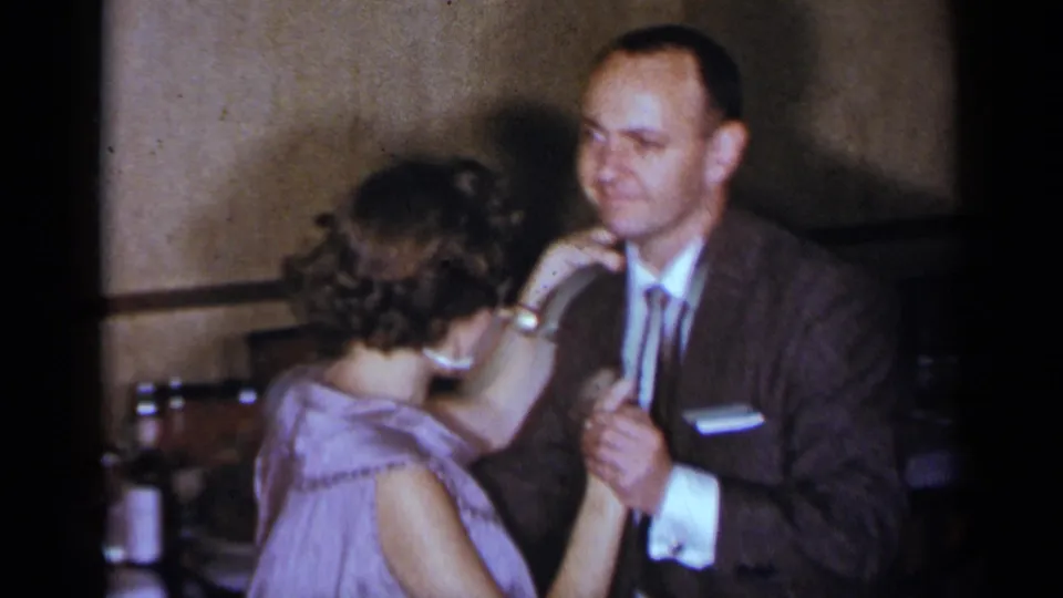 The woman in a lavender dress faces the suited man as they continue a close dance in the 1954 New York party interior.