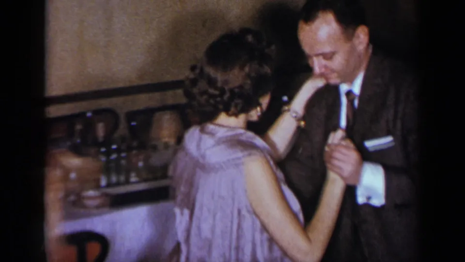 The woman turns her back toward the camera while dancing with the suited man inside the 1954 New York party setting.