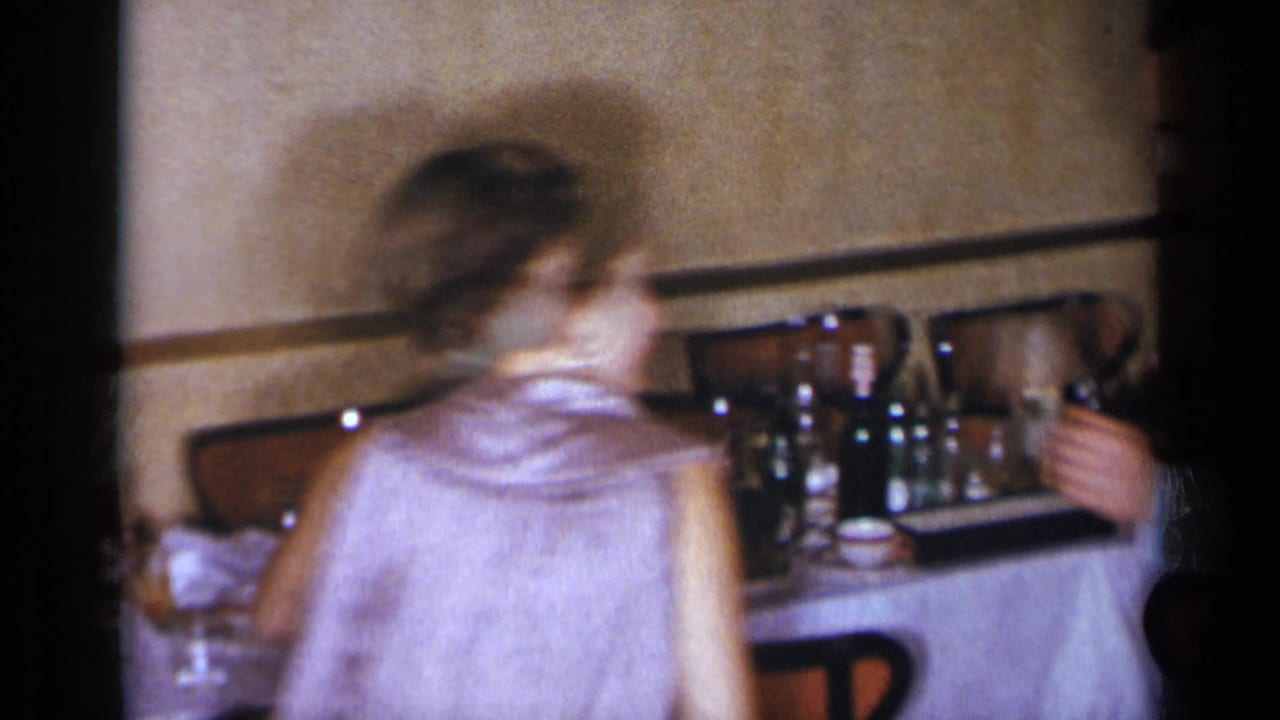 Woman in a light dress moves past a table with bottles and glasses.
